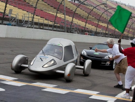 The Edison2 Very Light Car gets a green flag and thumbs-up at the Michigan International Speedway during Progressive Insurance Automotive X Prize trials. Edison2 has four cars in the X Prize Knockout stage.