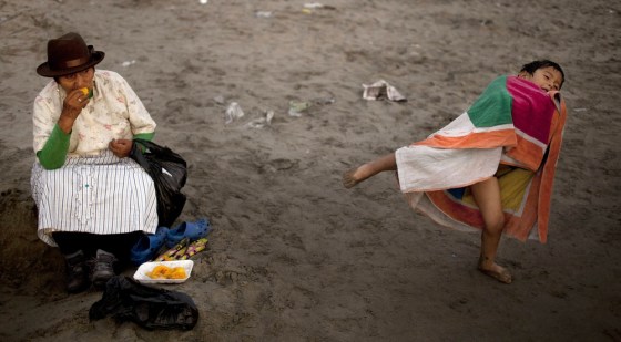 A woman snacks on mango fruit as her grandson plays nearby on Agua Dulce beach in Lima, Peru.
