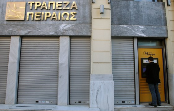 A man uses an ATM of Piraeus Bank in central Athens, Friday, March 22, 2013. Greece's Piraeus Bank said it has been chosen to buy two Cypriot banks' operations in Greece.