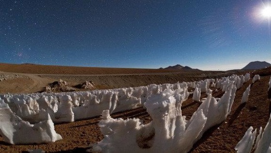 These bizarre ice and snow formations are known as penitentes (Spanish for 'penitents'). They are illuminated by the moonlight, which is visible on the right. On the left, higher in the sky, the Large and Small Magellanic Clouds can be faintly seen, while the reddish glow of the Carina Nebula appears close to the horizon on the far left. Photo by ESO Photo Ambassador Babak Tafreshi.