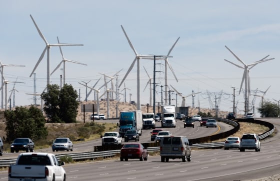 Automobiles pass by giant wind turbines powered by strong winds in Palm Springs, Calif.
