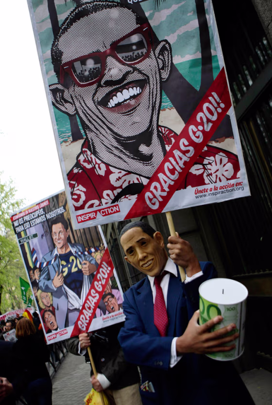 Man wearing mask depicting U.S. President Obama holds banner during demonstration against economic crisis and upcoming G20 meeting in Madrid