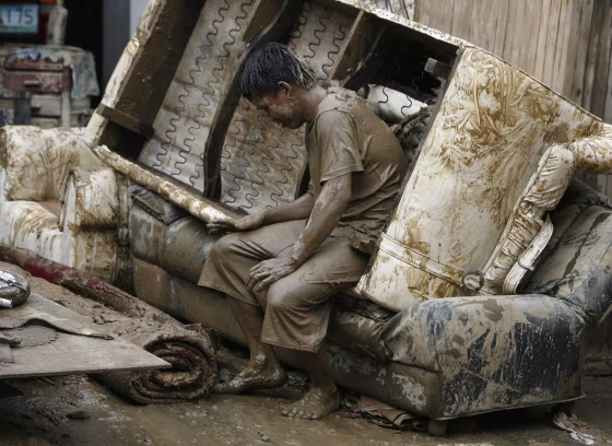 Image: A man takes a break from cleaning a house swamped by flash floods