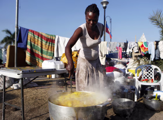 Image: A woman cooks soup in a large pot inside a displacement camp in Port-au-Prince