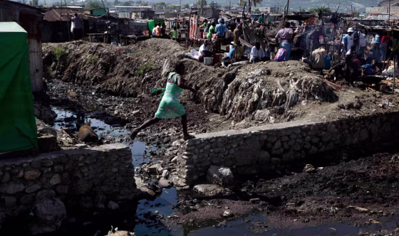 Image: A woman jumps along a wall near La Saline market in Port-au-Prince