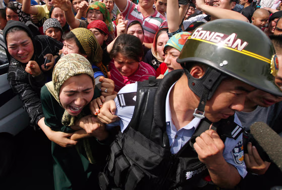 Image: A woman holds onto a Chinese policeman as a crowd of locals confront security forces along a street in the city of Urumqi