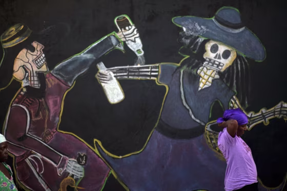 Image: A woman stands by a mural at the start of a Voodoo ritual for Fet Gede celebrations