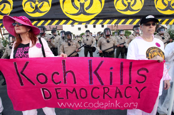 Image: Riverside County Sheriff's deputies in riot gear are seen behind Jodie Ivanes, of Venice Beach, Calif., left, and Ellen Sturtz, of West Los Angeles, right, during a protest dubbed the \"Koch Busters Rally\"