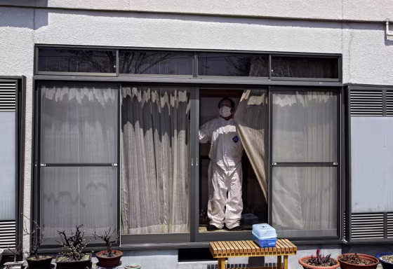 Image:A man, wearing a protective suite, shuts the curtains of a house in the deserted town of Futaba, inside the 20-kilometer (12-mile) evacuation zone, in Fukushima Prefecture, Japan