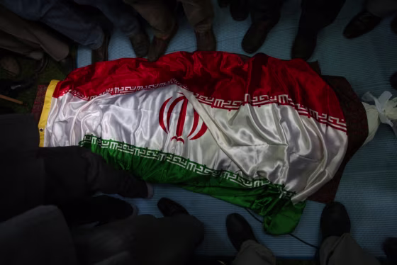 Image: Mourners stand around the flag draped body of Sahabi at his burial ceremony in Lavasan