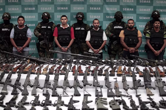 Image: Suspects are lined up as seized weapons are displayed to the media by the Mexican Navy in Mexico City