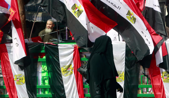 Image: A veiled Egyptian woman walks past Egyptian flags during a sit-in at Tahrir Square in Cairo