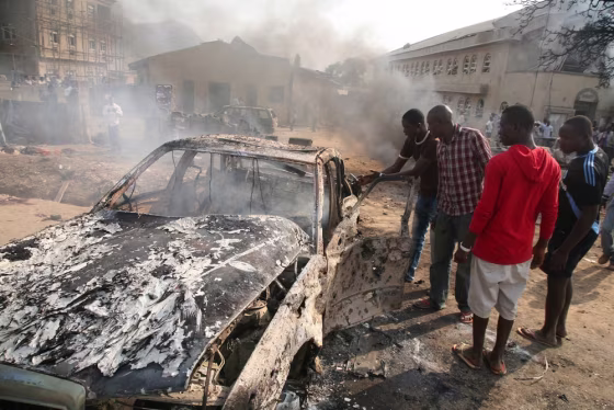 Image:Men look at the wreckage of a car following a bomb blast