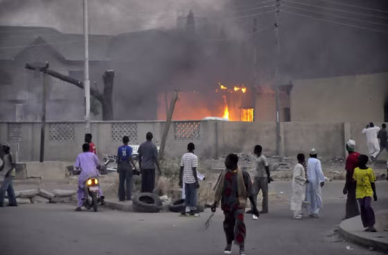 Image: People watch as smoke rises from the police headquarters after it was hit by a blast in Nigeria's northern city of Kano