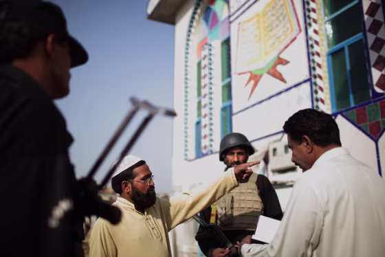Image: Police officers question a man in front of a mosque