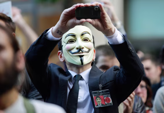 Image:A protester with the \"Occupy Seattle\" movement wears a mask and takes a photo with a mobile phone.