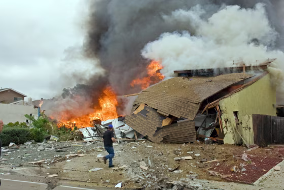 Man walks past burning debris after a military jet crashed into homes in San Diego