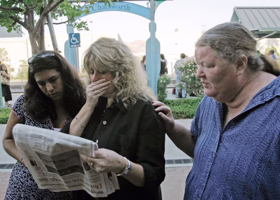 An unidentified commuter, left, and her companions, Melinda Moore, center, and Marianne Jones, right, react as they read names of fatalities from Friday's crash in the newspaper. They were waiting for a train Monday at the Chatsworth station.