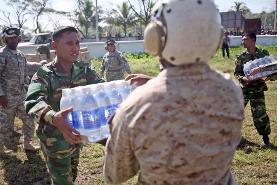 Image: U.S. Marine passes a Bangladeshi soldier a case of bottled water while unloading a shipment of food, water, and medical supplies