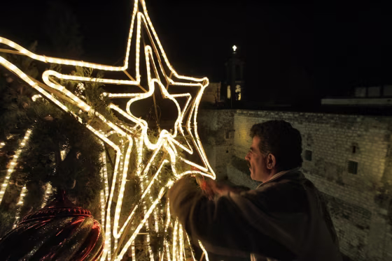 Image: A Palestinian municipal worker fixes the \"star of Bethlehem\" on top of the central Christmas tree in Manger Square outside the Church of the Nativity.
