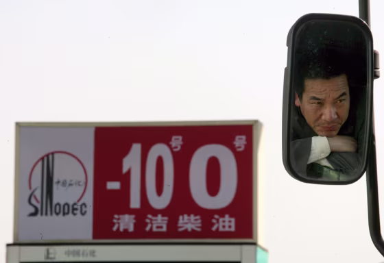 Image: A Chinese truck driver is seen in a back mirror while waiting outside a Sinopec gas station.