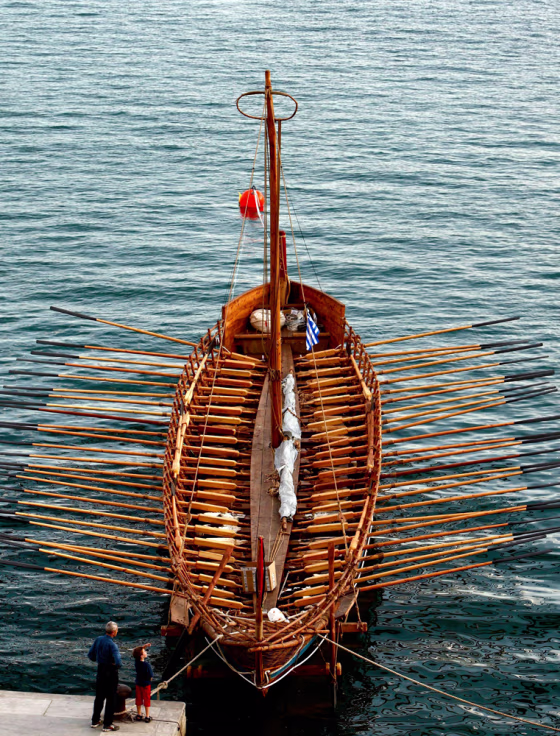 A man and a child look at the Argo replica ship docked at the port of Volos town in central Greece