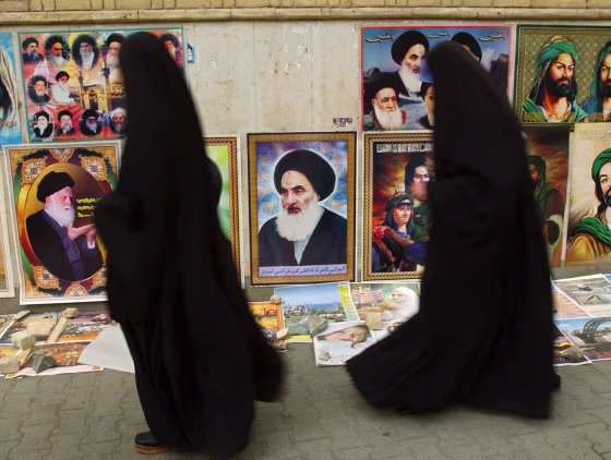 Two Iraqi women walk past a portrait of Grand Ayatollah Ali al-Husseini al-Sistani, center, in Baghdad on Tuesday.&nbsp;Al-Sistani's support for a U.S.&nbsp;transition plan is&nbsp;seen as crucial for its&nbsp;success.