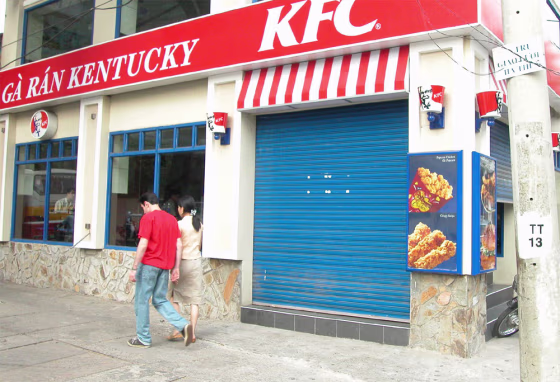 PEDESTRIANS WALK PAST A SHUTTERED KENTUCKY FRIED CHICKEN RESTAURANT IN HO CHI MINH CITY