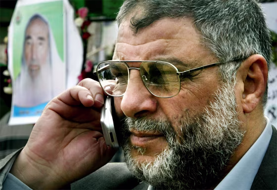 Abdel Aziz Rantisi talks on a cell phone Tuesday while taking part in the mourning procession in Gaza City for slain Hamas&nbsp;leader Sheik Ahmed Yassin, seen&nbsp;in the poster.