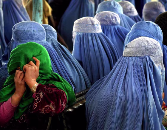 A young girl joins the crowd of burka-clad women by hiding her face at the site of a male visitor at a medical clinic in Karabagh.