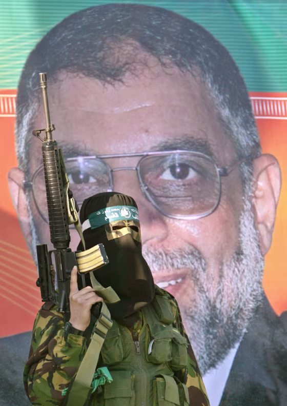 MASKED PALESTINIAN HAMAS MILITANT MARCHES IN FRONT POSTER OF SLAIN HAMAS LEADER ABDEL AZIZ AL-RANTISSI AT KHAN YOUNIS REFUGEE CAMP