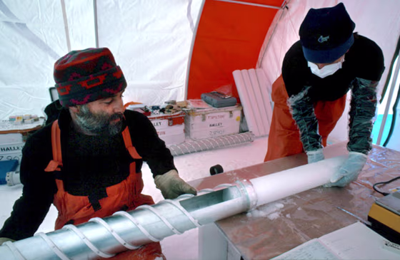 Researchers remove ice core from a drill at their remote Antarctic station.