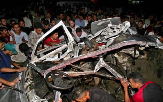 Palestinians surround a destroyed car after it was hit by a missile in Gaza