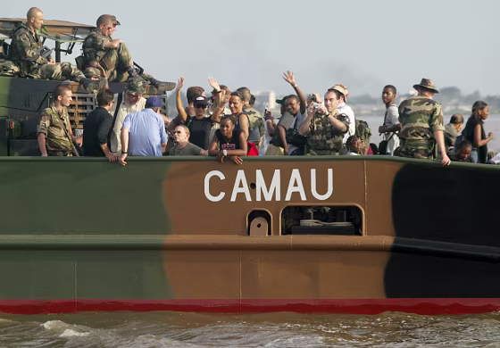 Foreigners traveling by boat wave Saturday as they leave for the airport&nbsp;at Abidjan, Ivory Coast. The foreigners, many of them longtime Ivory Coast residents, piled into buses, boats and planes Saturday as a French-run evacuation built despite government promises to quell a surge of anti-French violence. 