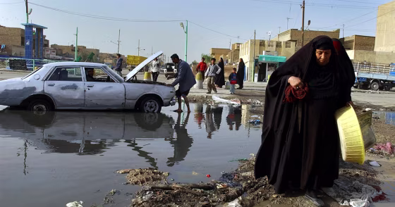 A woman walks past a man fixing his car in a flooded street in Baghdad's Shiite enclave of Sadr City last month.