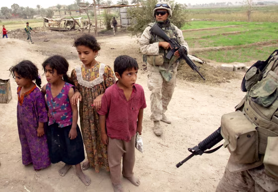 Iraqi children look on as U.S. Marines&nbsp;search the area outside Fallujah last October.