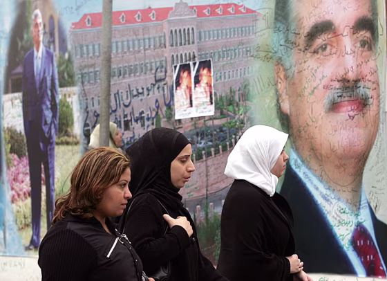 Lebanese women pass a mural of Lebanon's slain former prime minister Rafik Hariri covered with poems and condolences from wellwishers near his grave in Beirut, on Sunday. At his funeral, Christians, Muslims and Druse came together in a vivid manifestation of unity rare in Lebanon's violent, sectarian-charged history.