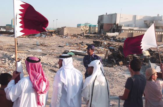 Demonstrators&nbsp;holding Qatari flags walk past the site of Saturday's car bombing during a protest rally against the blast, Monday.