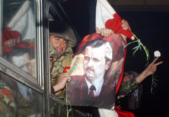 Syrian troops withdrawing from Lebanon display Syrian flags along with posters of President Bashar Assad as they cross the Syrian-Lebanese border early Saturday.