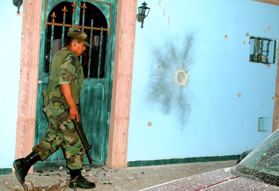 A Mexican soldier walks past a house riddled with bullet holes in Nuevo Laredo