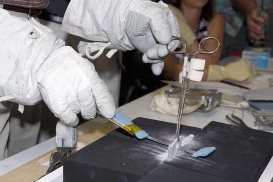 An engineer wearing astronaut gloves tries out a technique to cut away a protruding strip of gap-filler material while holding it steady with a forceps. Astronaut Stephen Robinson may use a similar technique on Discovery during a Wednesday spacewalk.