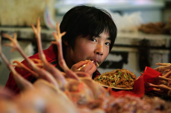 A young Chinese man eats next to freshly killed chickens at his chicken stall in a Beijing market on Oct. 28.