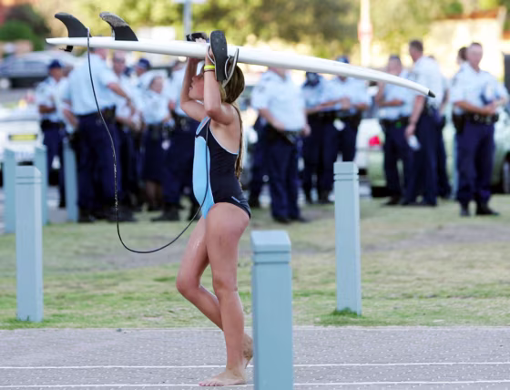 Young surfer carries her board on her head as she passes a group of police officers outside North Cronulla Surf Club in Sydney