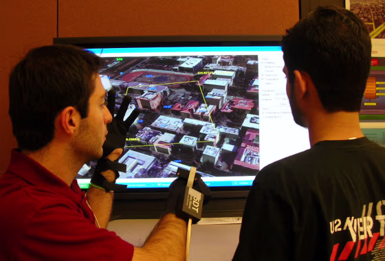 University of Southern California graduate student Jeff Khoshgozaran, at left,&nbsp;gestures with data gloves to zoom in on an area on the screen he wants to see in more detail. The glove interface is recognized by the Geospatial Decision Making database, or GeoDec.