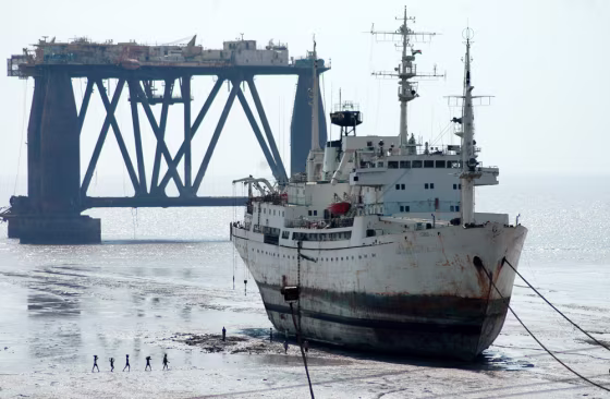 Workers walk past a ship and an oil drilling rig, both waiting to be dismantled at a ship breaking yard in Alang, in the western India. After spending 20 to 30 years on the high seas, ships some as tall as 15-story buildings and as long as several football fields, make their way to beaches across India and&nbsp;Bangladesh to be dismantled.