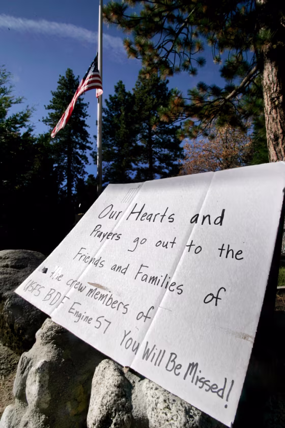 The U.S. flag flies at half-staff behind a sign in memory of four firefighters who died and one who was injured in the Esperanza fire at a roadside memorial near Idyllwild, Calif., on Saturday.
