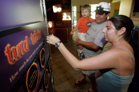 Stephanie Rey, right, tests her skill at "turd trivia" as she, her father, Gustavo Rey, and her son, Phillippe Mann, tour an exhibit on excrement titled "The Scoop on Poop" at Miami Metrozoo in Miami. 