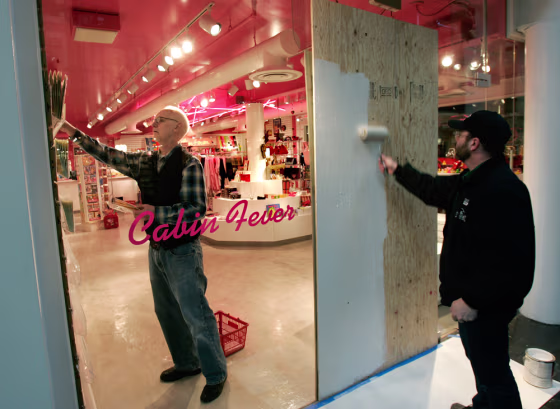 A&nbsp;worker paints a sheet of plywood as a temporary repair to a plate glass window that was shot out as a store employee restocks a gift store in Trolley Square mall on&nbsp;Wednesday.