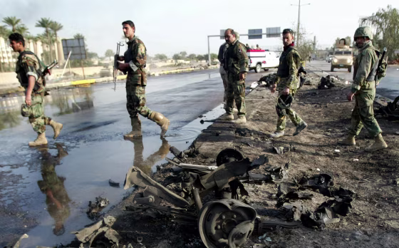 Iraqi army soldiers walk past car wrecka