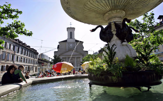 A mother relaxes with her child on a well at the Place du Marche in the heart of Carouge, a suburb of Geneva. Place du Marche is still used as a marketplace and starting point for random exploration of the quarter.